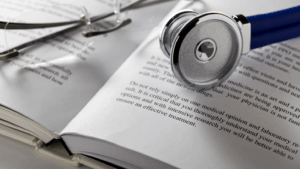 Primo piano di uno stetoscopio poggiato su un libro aperto, accanto a un paio di occhiali da lettura. L'immagine rappresenta il legame tra conoscenza medica, ricerca scientifica e pratica clinica.