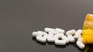 Pillole bianche fuoriuscite da un flacone su sfondo nero, simbolo della dipendenza da oppiacei e da trattamenti farmacologici.